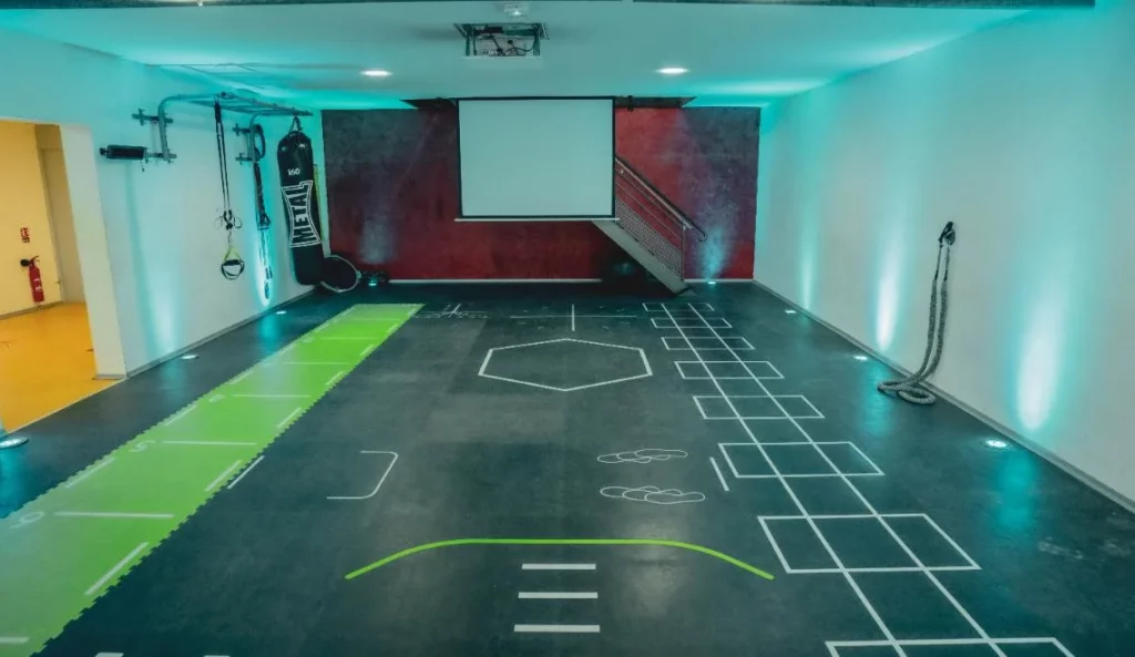 Salle d’entraînement fonctionnel IPMS avec marquages au sol et mur rouge.