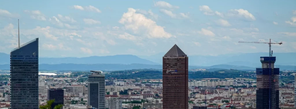Vue panoramique du quartier de la Part-Dieu à Lyon avec ses tours emblématiques et les Alpes en arrière-plan.