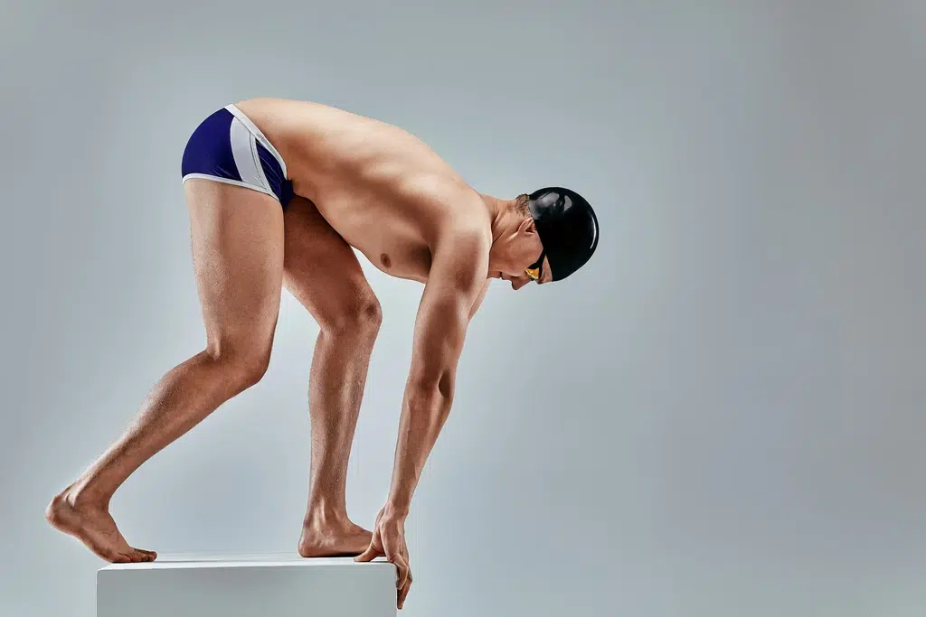 Nageur en position de départ sur plot prêt à plonger avec bonnet et lunettes de natation