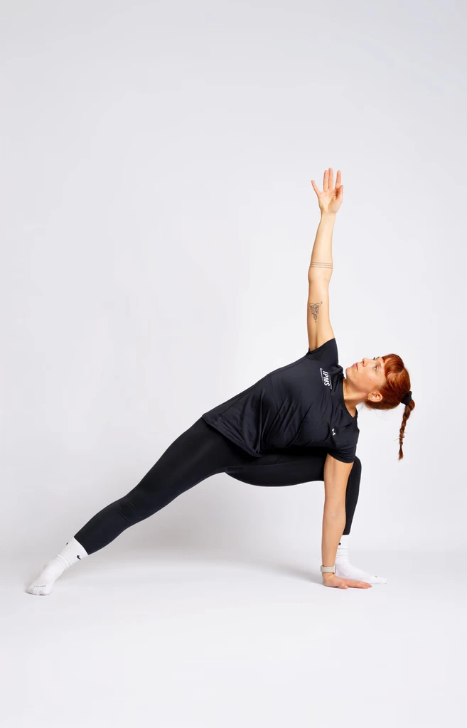 Stagiaire IPMS en tenue noire réalisant une posture de stretching avec rotation et bras tendu