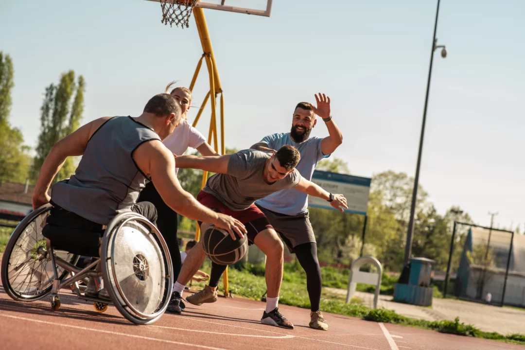 Séance de basket inclusif réunissant des joueurs valides et un joueur en fauteuil sur terrain extérieur.