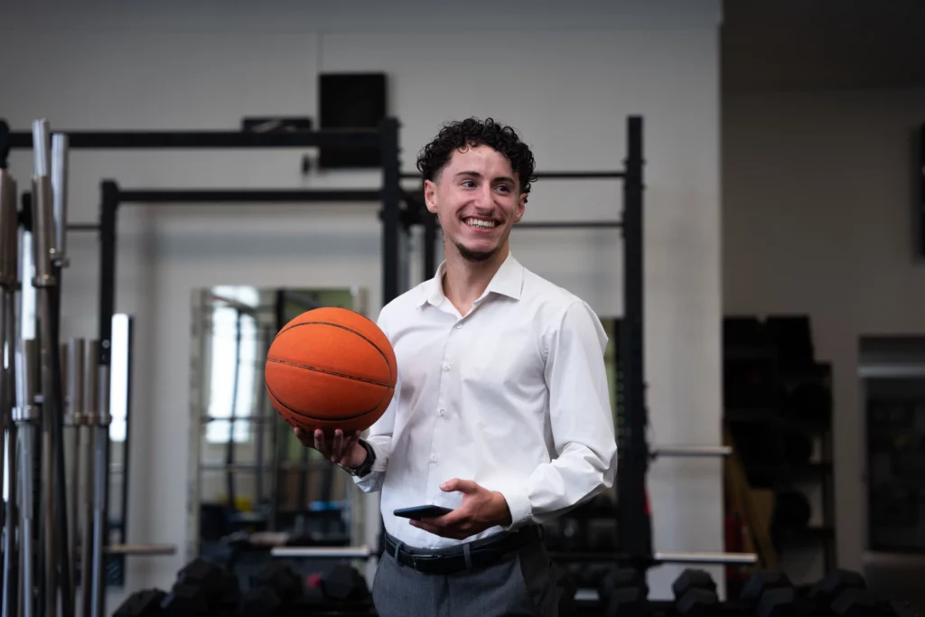 Futur technico-commercial du sport tenant un ballon de basket dans un espace de musculation, symbolisant l’univers sportif lié au commerce.