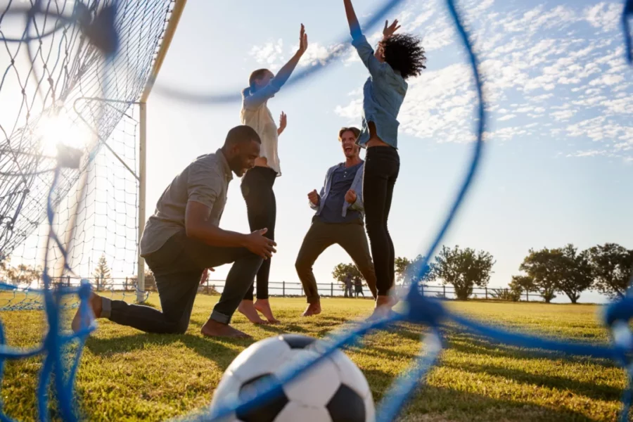 Groupe d’adultes célébrant un but lors d’une séance de football loisir en plein air.