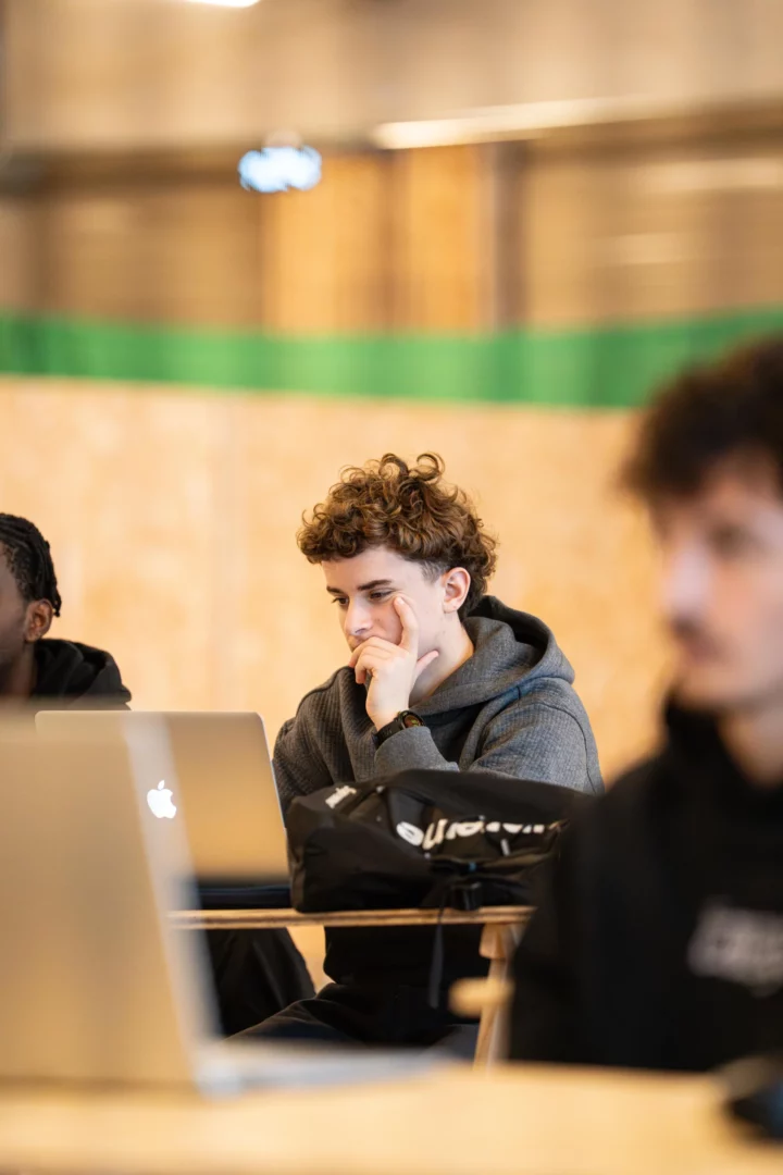 Étudiant en formation technico-commercial réalisant une veille commerciale sur ordinateur en salle de cours.